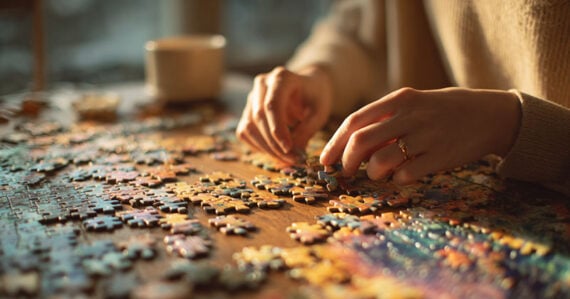 Photo of human hands assembling a jigsaw puzzle on a table Photo of human hands assembling a jigsaw puzzle on a table
