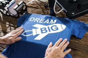 Image of a t-shirt being printed with the words "Dream Big"