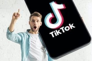 Photo of a young male holding a smartphone with TikTok app on it